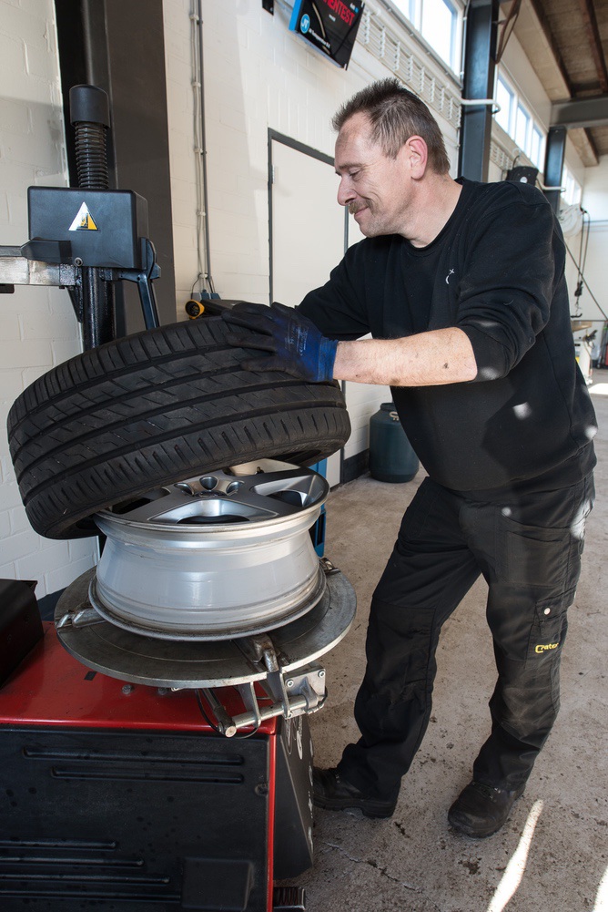 Monteur met een band en velg in de werkplaats van Beil Auto